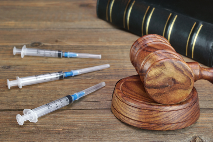 photo of a judge gavel and law book from a courtroom next to illegal drug needles