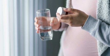 woman holding glass of water and pill bottle