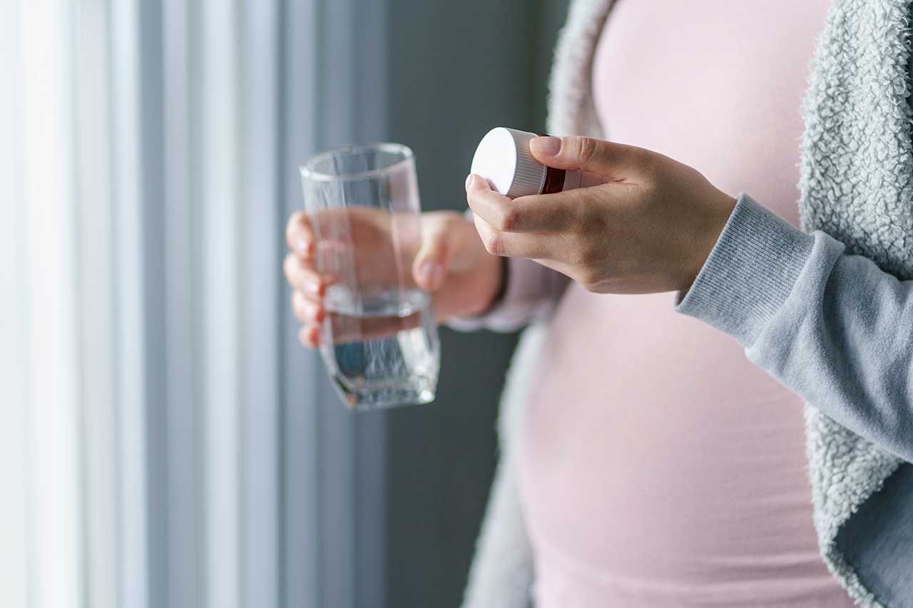 woman holding glass of water and pill bottle